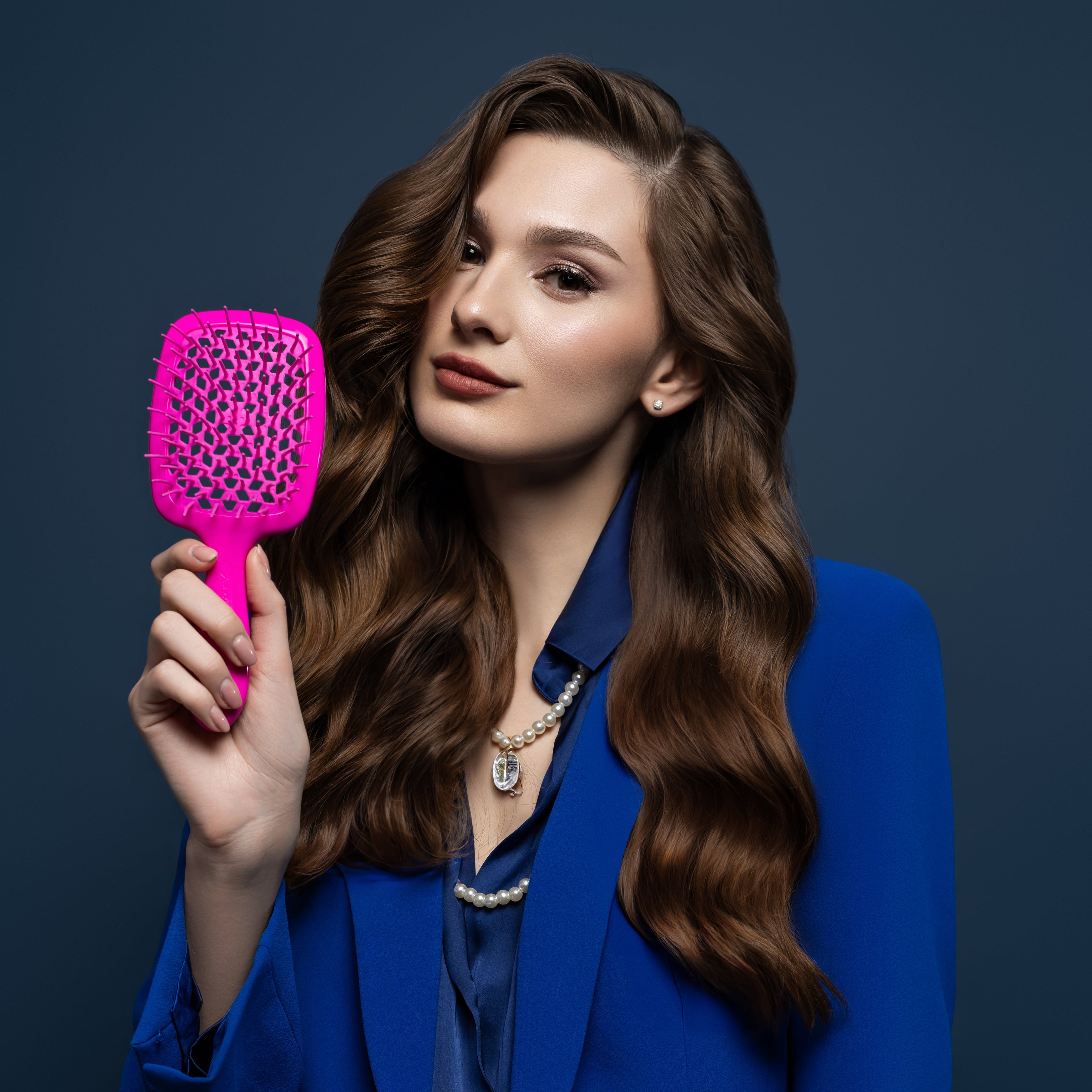 Woman in a blue suit holding a pink hairbrush against a dark background