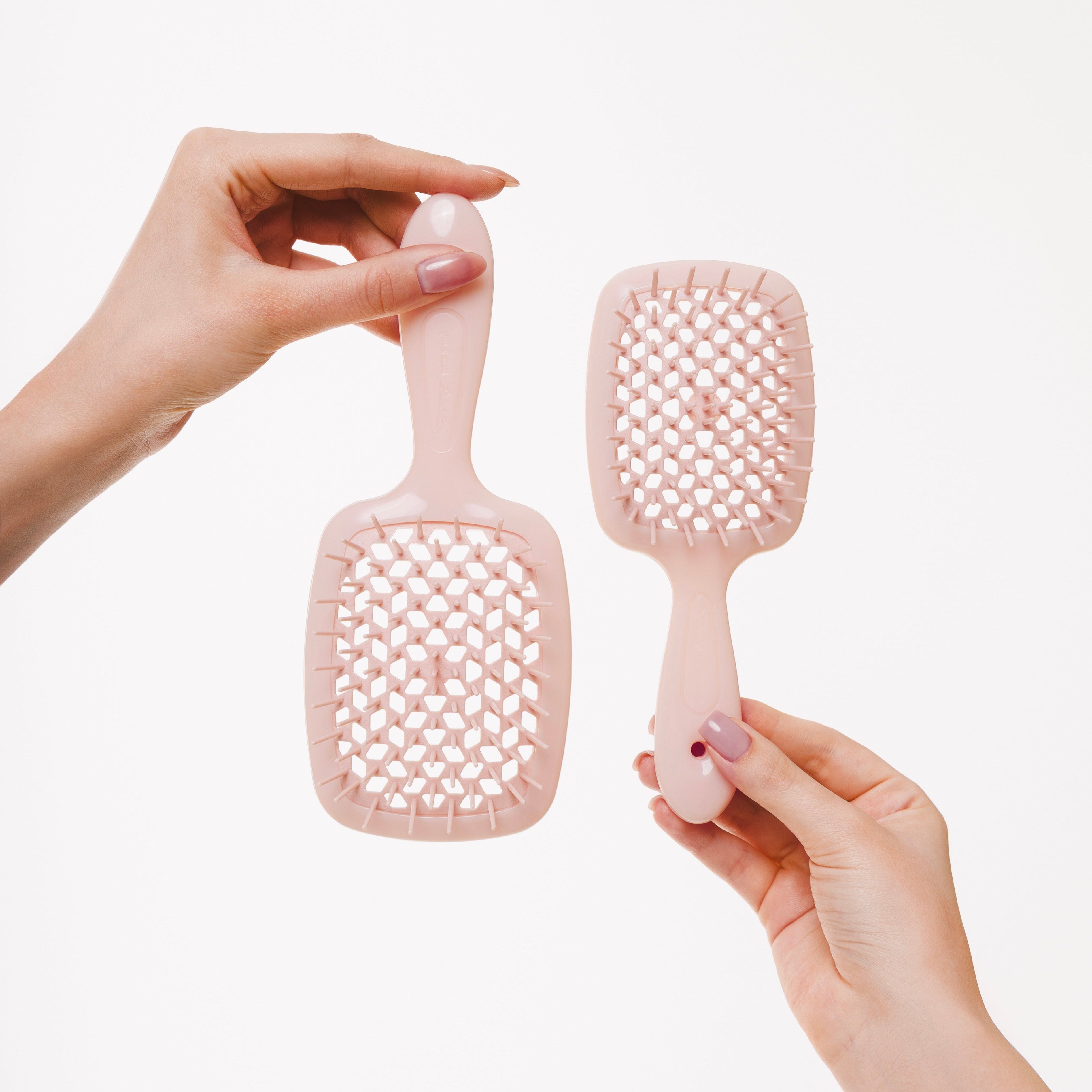 Two pink pet grooming brushes held by hands against a white background